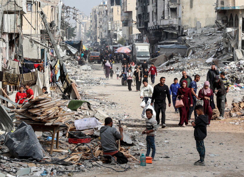Persone che camminano tra le macerie di edifici crollati e danneggiati lungo una strada di Gaza City.