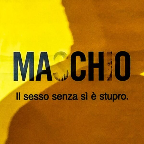 L'ombra di un uomo si staglia su un manifesto giallo con la scritta nera "Maschio" in cui le lettere che compongono il sì spariscono trasformando la parola in "macho"