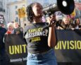 persona con megafono davanti a striscioni durante una protesta